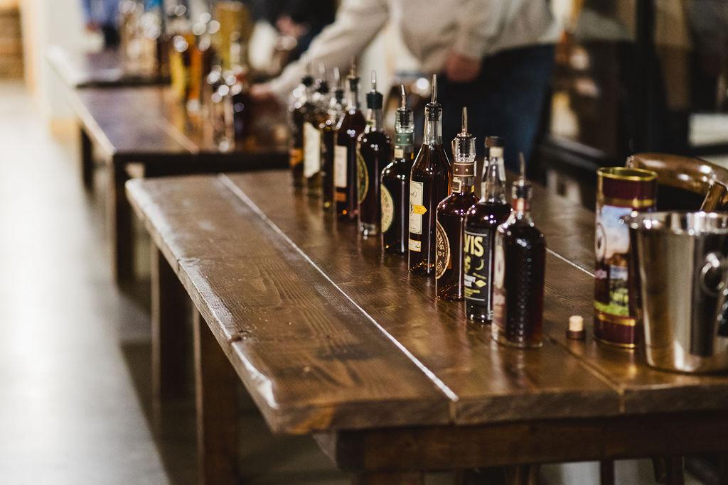 Bourbon tasting table lined with premium whiskey bottles at the Bourbon & Bacon Social at The Meadow Barn in Harrisburg, South Dakota